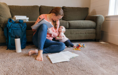 A mother and parent sits with her baby daughter on the family room floor studying for a university class. She is a hard working college student trying to earn her degree in education to improve her situation.